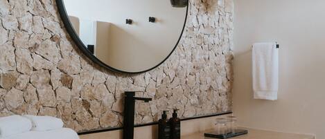 A bathroom with a stone wall, a round mirror, a sink, and two pendant lights.