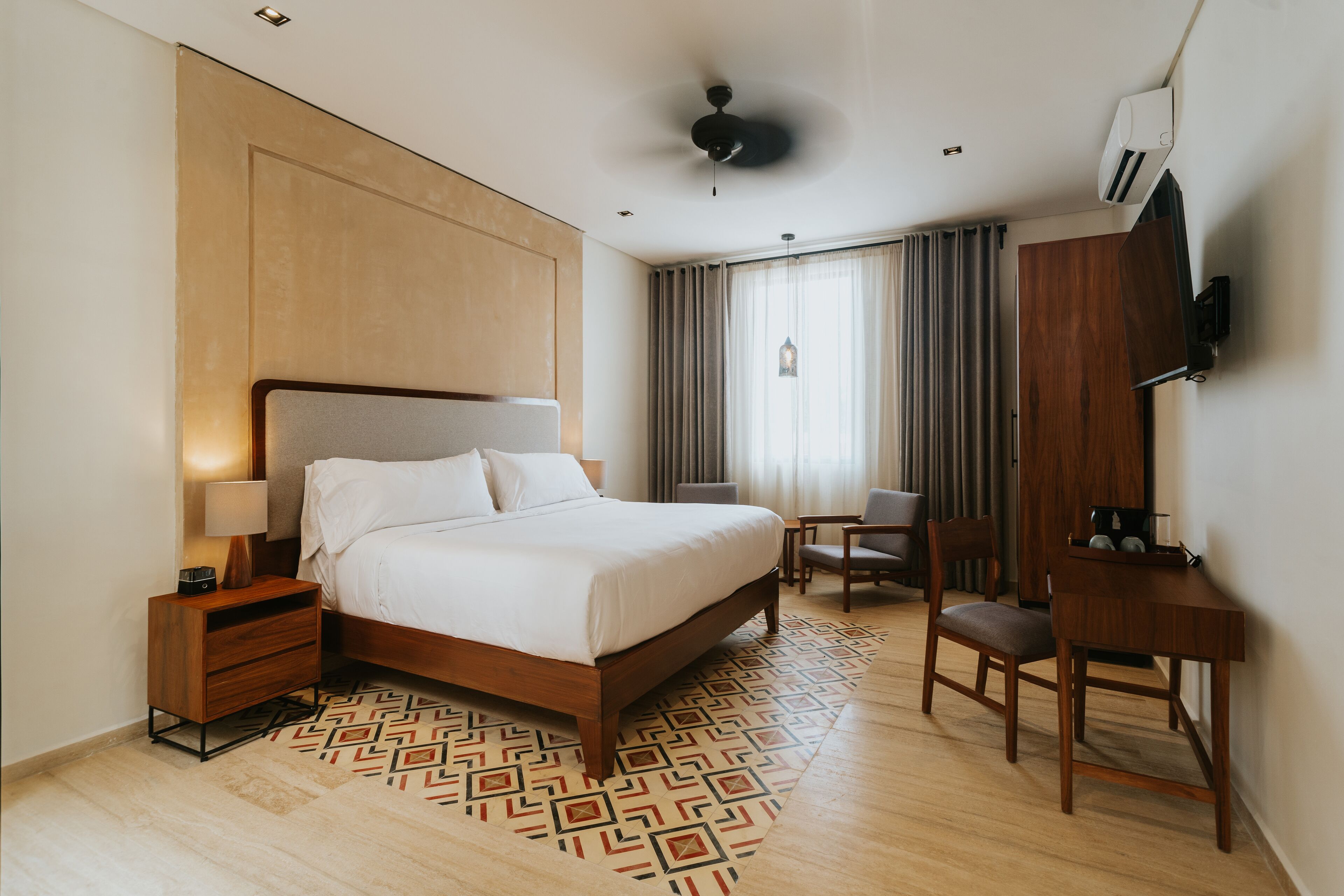 Ein Hotelzimmer mit Bett, Nachttisch, Lampe, Schreibtisch, Stuhl und einem an der Wand befestigten Fernseher.