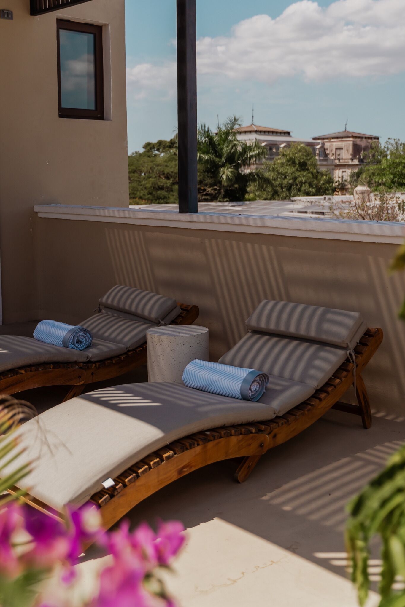 Two lounge chairs with cushions, a small table, and a view of buildings and trees in the background.