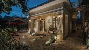 Un espacio exterior bien iluminado con un patio, asientos y una escalera que conduce a la entrada.