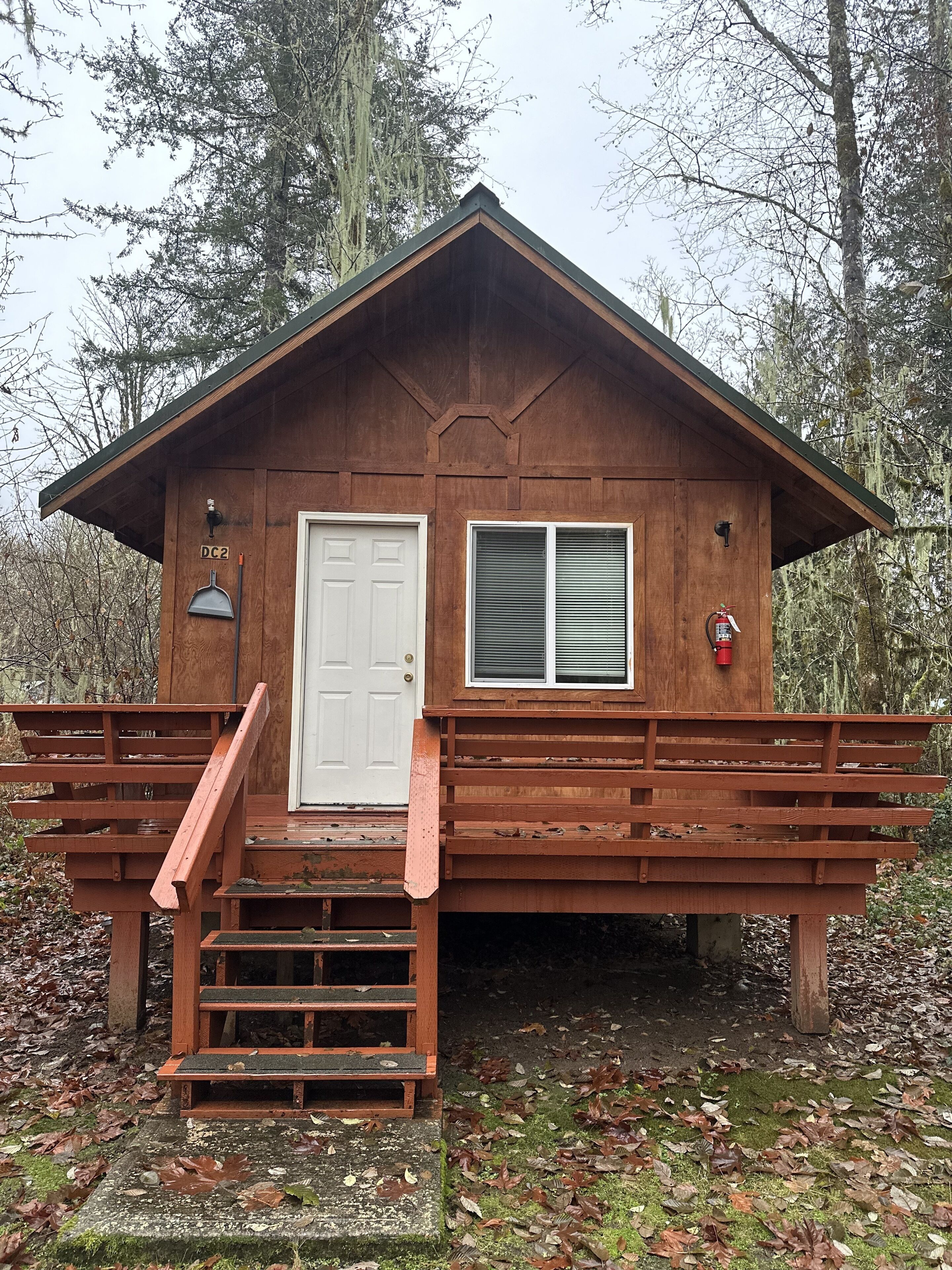 A wooden cabin with a white door, a window, and a fire extinguisher.