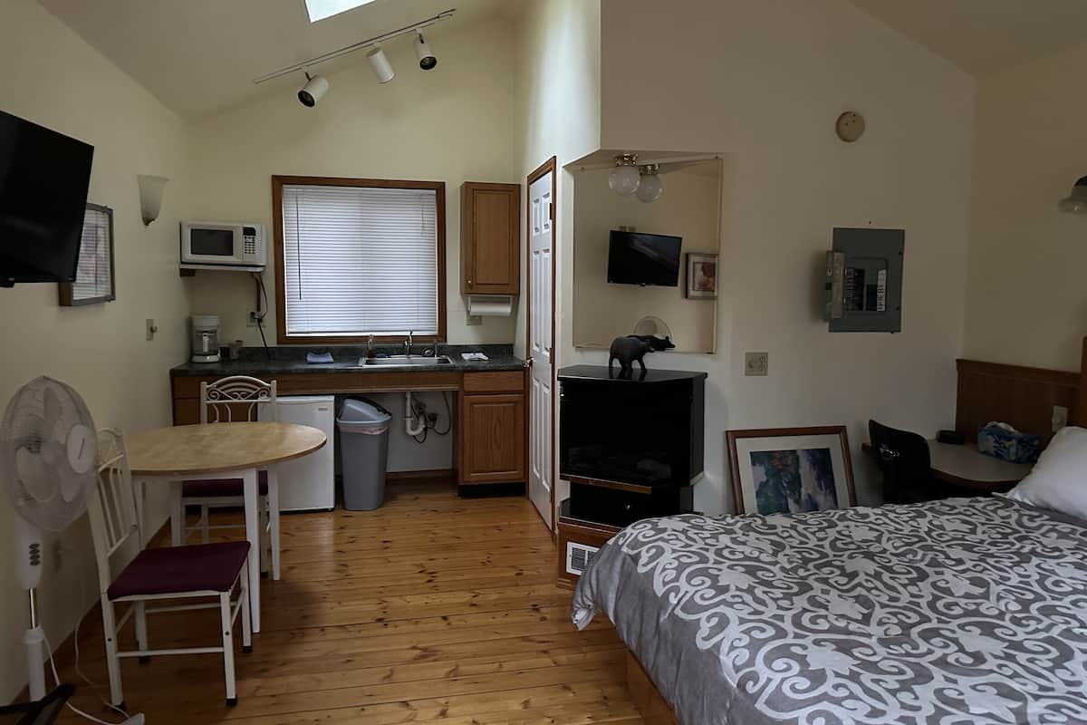 A compact room with a kitchenette, a bed, a desk, and a TV.