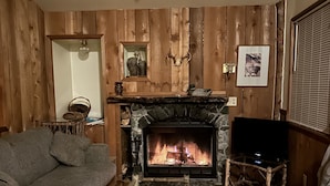 Una sala de estar acogedora con chimenea de piedra, paredes de madera, un sofá gris y una mesa de centro rústica.