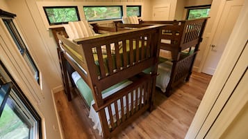 A room with bunk beds, a television, and windows with a view of greenery.