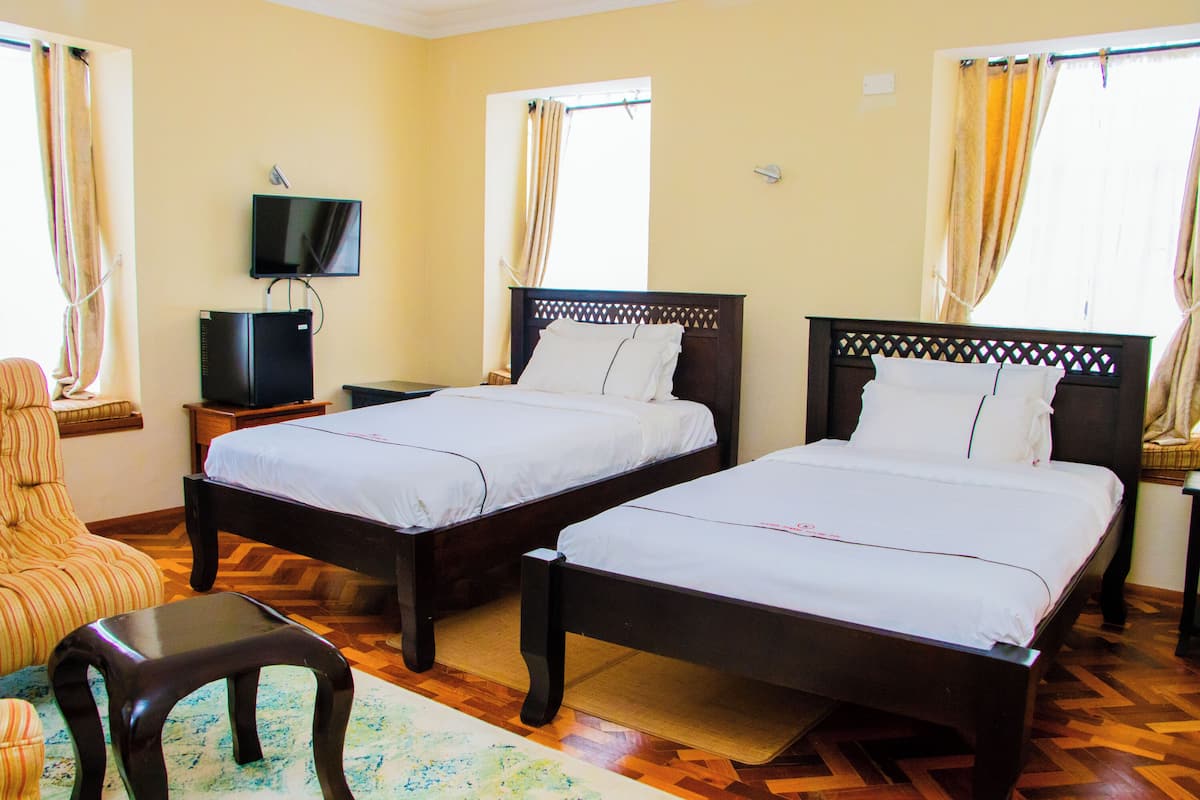 A hotel room with two single beds, a television on a stand, a wooden floor, and curtains on the windows.