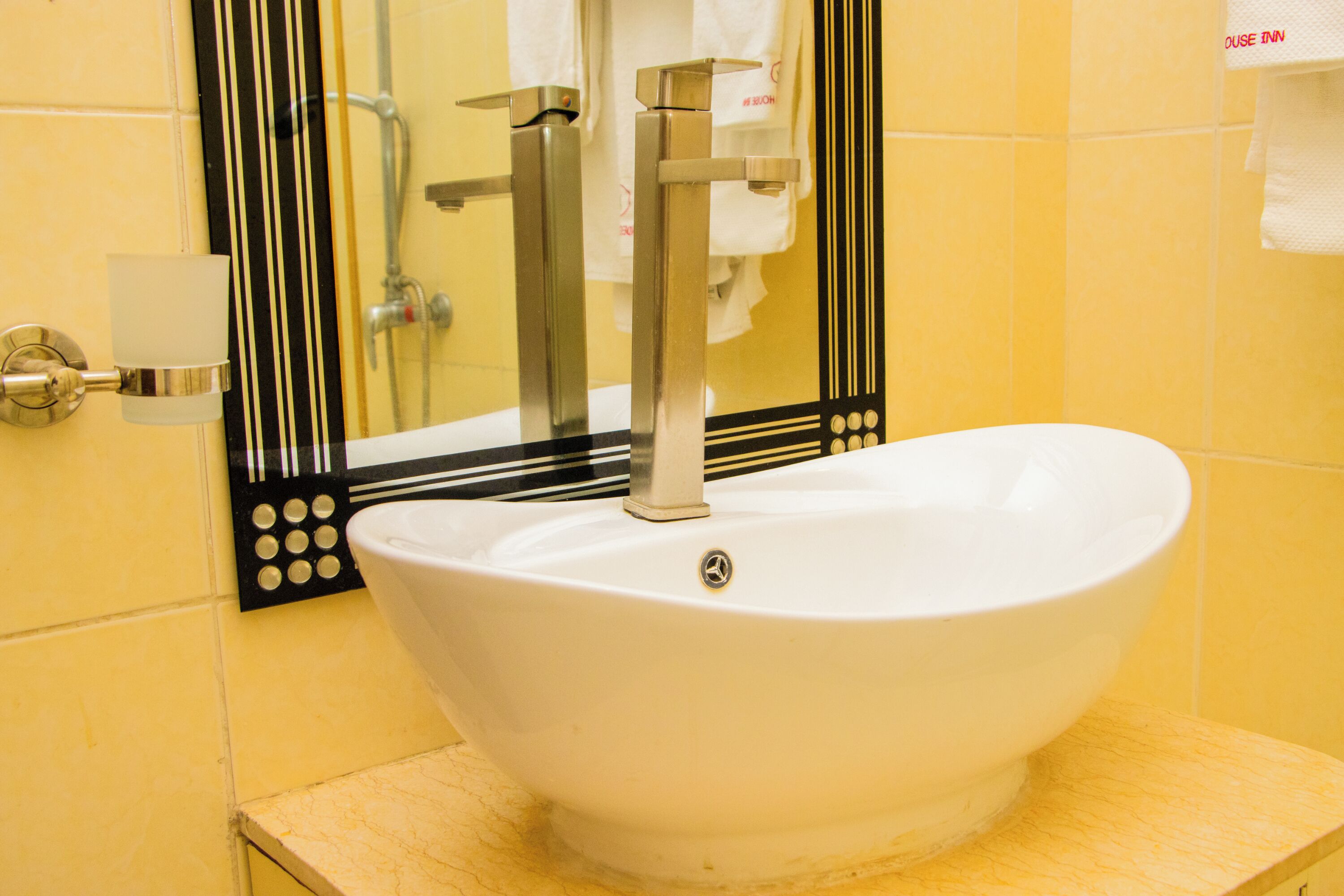 A bathroom with a white sink, a mirror with a black frame, and yellow tiled walls.