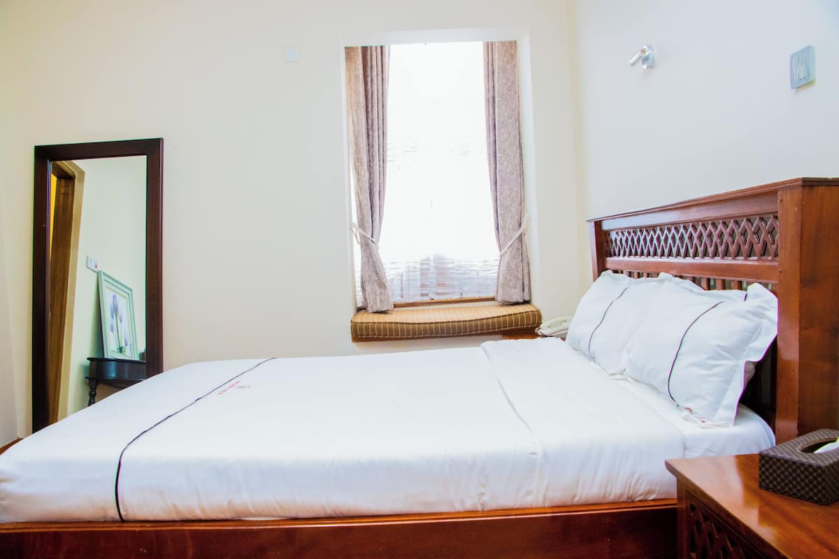 A neatly made bed with a wooden headboard, a window with curtains, and a bedside table with a tissue box.