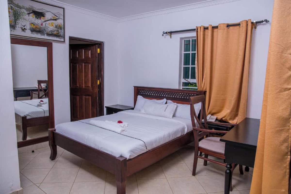 A neatly arranged bedroom with a wooden bed, a chair, a desk, and a window with curtains.