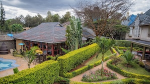 A landscaped garden with a swimming pool, a covered outdoor seating area, and a building with a tiled roof. - Blixen Resort & Spa  (Nairobi)