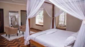 A room with a bed, two armchairs, a mirror, and a window with a view. - Blixen Resort & Spa  (Nairobi)