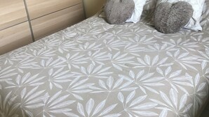 Una cama con una colcha estampada con hojas, dos almohadas y un armario de madera.