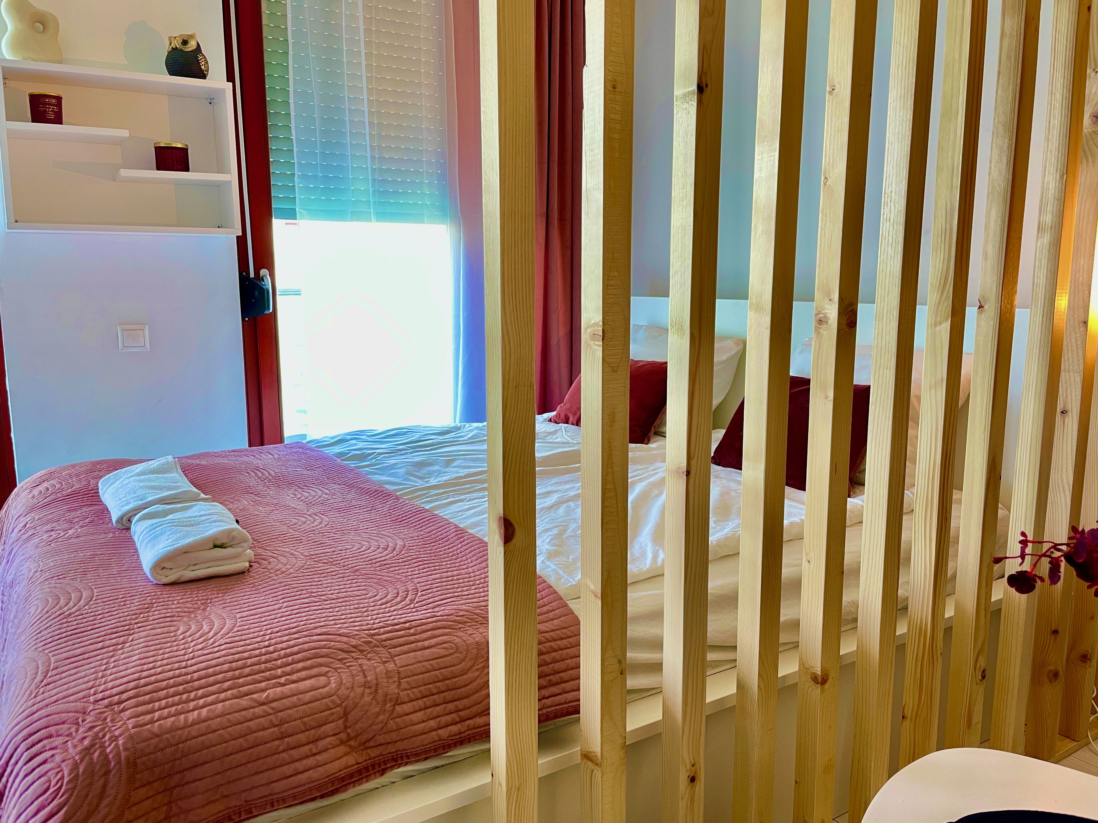Ein Schlafzimmer mit einem Bett, einem Nachttisch, einem Fenster mit Vorhängen und einem Regal mit Dekoration.