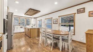 Une cuisine avec un plancher en bois, des armoires blanches, une table à manger en bois avec des chaises et un îlot central intégré doté d’un évier.