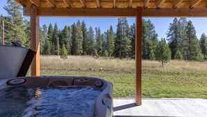 Un bain à remous sous une pergola en bois, avec vue sur un champ verdoyant et des arbres.