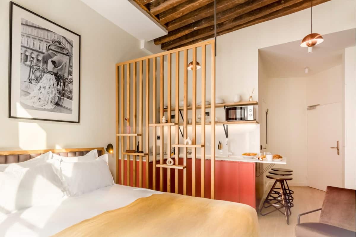 Une chambre d’hôtel moderne comprenant un lit, une cloison en bois, un coin cuisine et un espace repas.