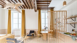 Eine moderne Küche mit Holzbalken, einem Essbereich mit rundem Tisch und einer Kücheninsel mit Obst und Glaswaren.