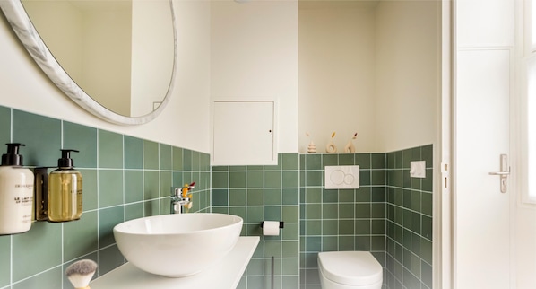Une salle de bain avec un grand lavabo blanc, des carreaux verts, un miroir et des articles de toilette accrochés au mur.