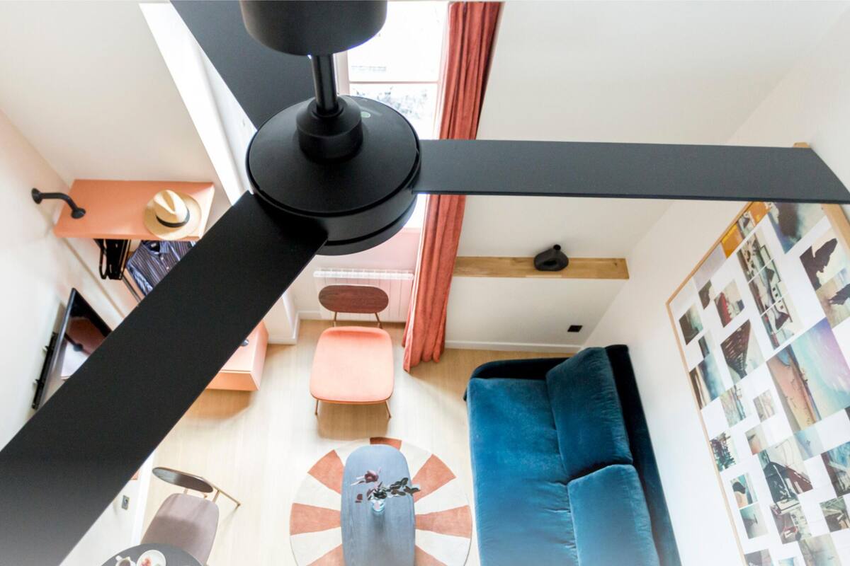 Un ventilateur de plafond, un canapé bleu, une table basse et un mur orné de photographies.