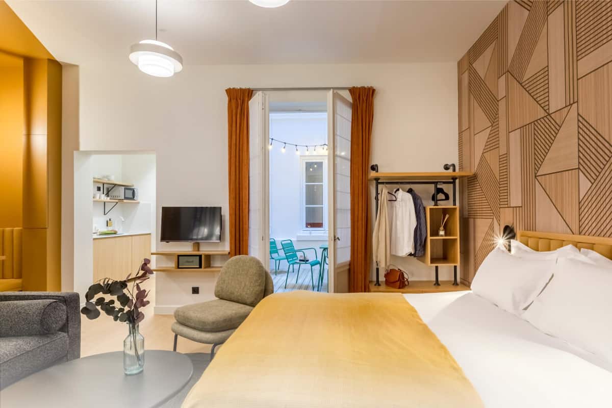 Une chambre d’hôtel avec un lit, une télévision, une petite table avec un vase, une chaise et une armoire.