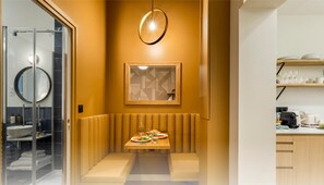 Ein modernes Badezimmer mit Duschkabine aus Glas, einem runden Spiegel und einer beigefarbenen Sitzbank mit kleinem Tisch.