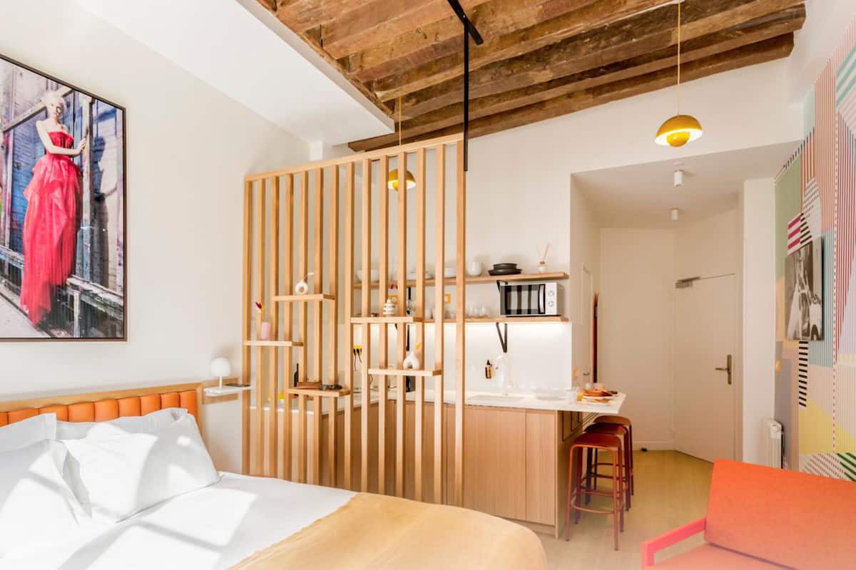Une chambre d’hôtel moderne comprenant un lit, une cloison en bois, un coin cuisine et un mur aux couleurs vives.