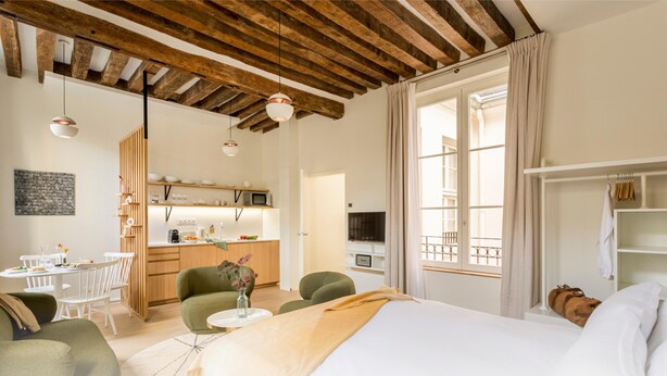 Ein modernes Hotelzimmer mit Holzboden, einem Bett, einem Essbereich und einer Küche.