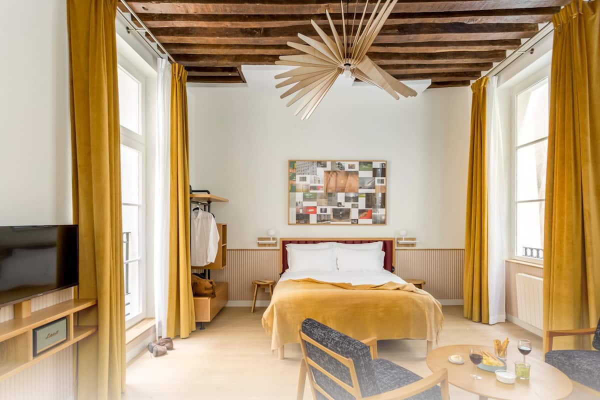 Une chambre moderne comprenant un lit, deux fauteuils, une table, un téléviseur et un luminaire au plafond au design original.