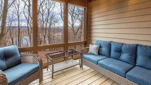 A covered porch with wicker furniture, a glass table, and a view of trees and a body of water. - Rock Cove Villa | 3 Kings + Private Baths | Walk to Golf · Fireplace · Foosball (Galena)
