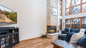 A living room with a fireplace, a television, and a stone wall. - Rock Cove Villa | 3 Kings + Private Baths | Walk to Golf · Fireplace · Foosball (Galena)