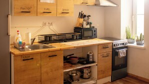 A compact kitchen with wooden cabinets labeled for organization, a microwave, a stove, and a sink. - Lighthouse Hostel & Rooms (Riga)