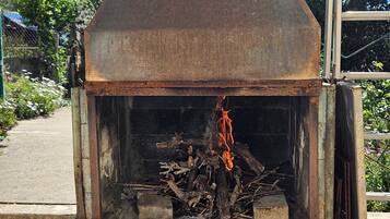 Un forno a pizza rustico all'aperto con canna fumaria, circondato da vegetazione e una scala in metallo.