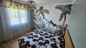 Une chambre à coucher avec un lit, une fenêtre ornée de rideaux légers, une fresque murale représentant un arbre et un luminaire suspendu.