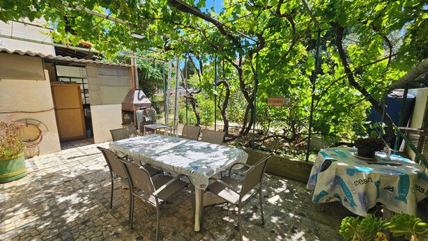 Une terrasse extérieure avec une table et des chaises, entourée de verdure et dotée d’un sol en briques.