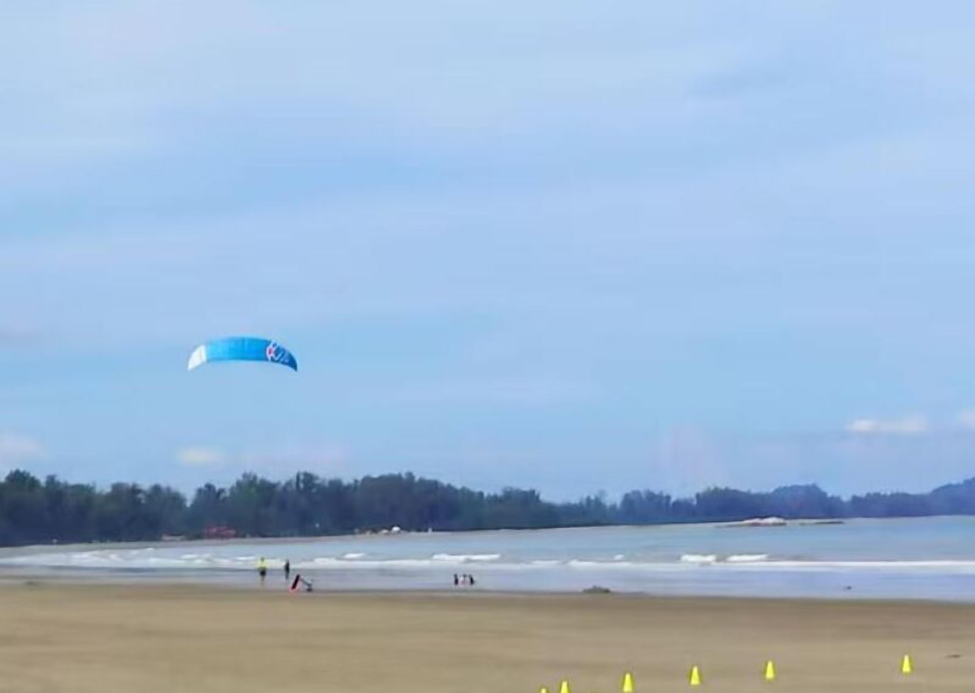 Una playa con una cometa azul volando en el cielo.