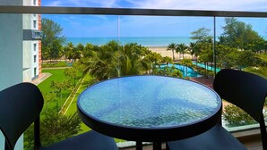 A balcony with a glass table and chairs, overlooking a beach and pool area. - Timurbay Seafront Residences NatureHome (Kuantan)