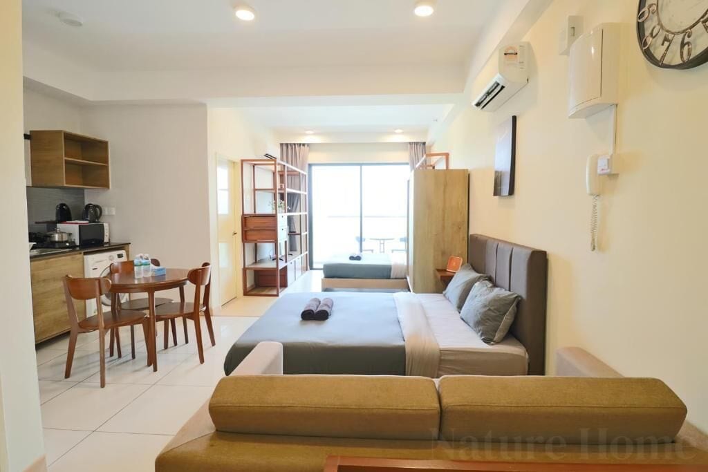 A modern hotel room with a bed, a sofa, a dining area with a table and chairs, and a kitchen area.