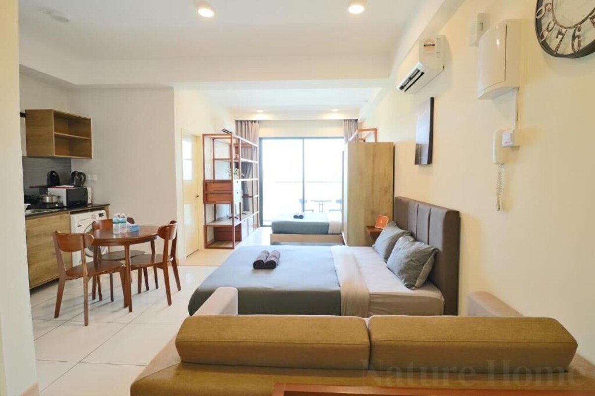 A modern hotel room with a bed, a sofa, a dining area with a table and chairs, and a kitchen area.