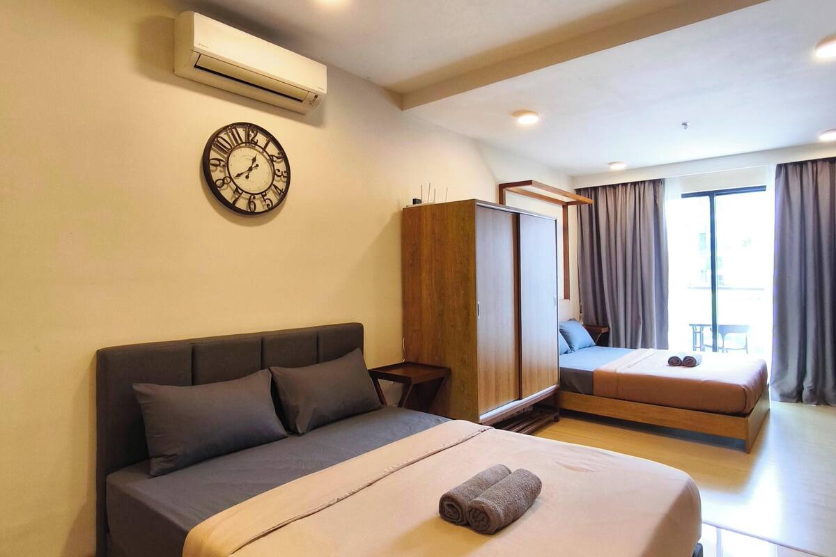A hotel room with a large bed, a wardrobe, a small table, and a window with curtains.