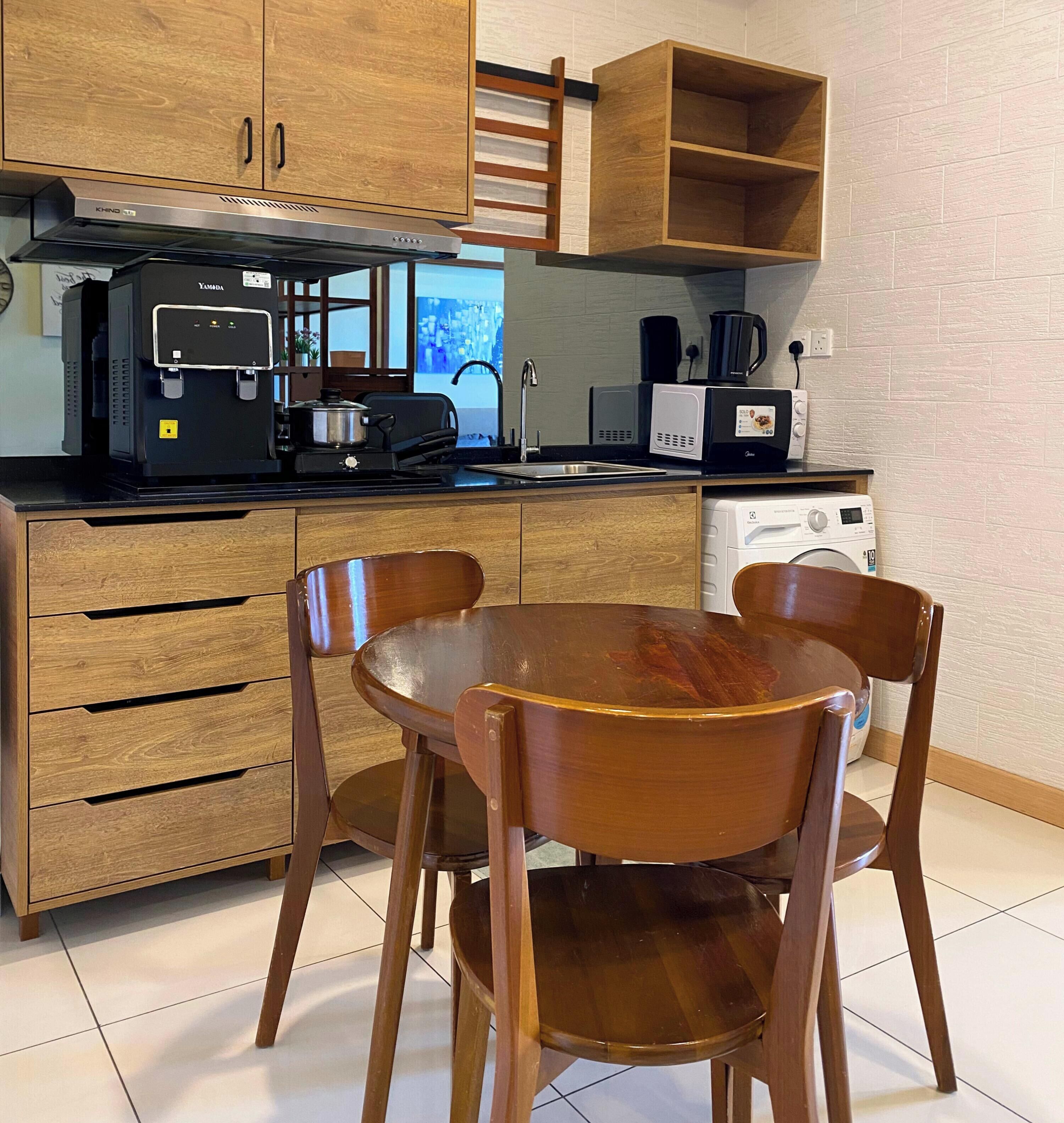 A compact kitchen with wooden cabinets, a built-in stove, a microwave, and a coffee maker. There is a dining table with four chairs.