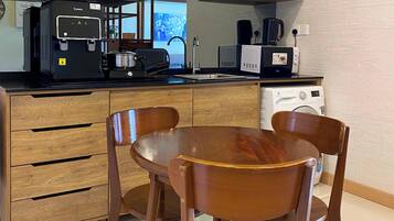 A compact kitchen with wooden cabinets, a built-in stove, a microwave, and a coffee maker. There is a dining table with four chairs.