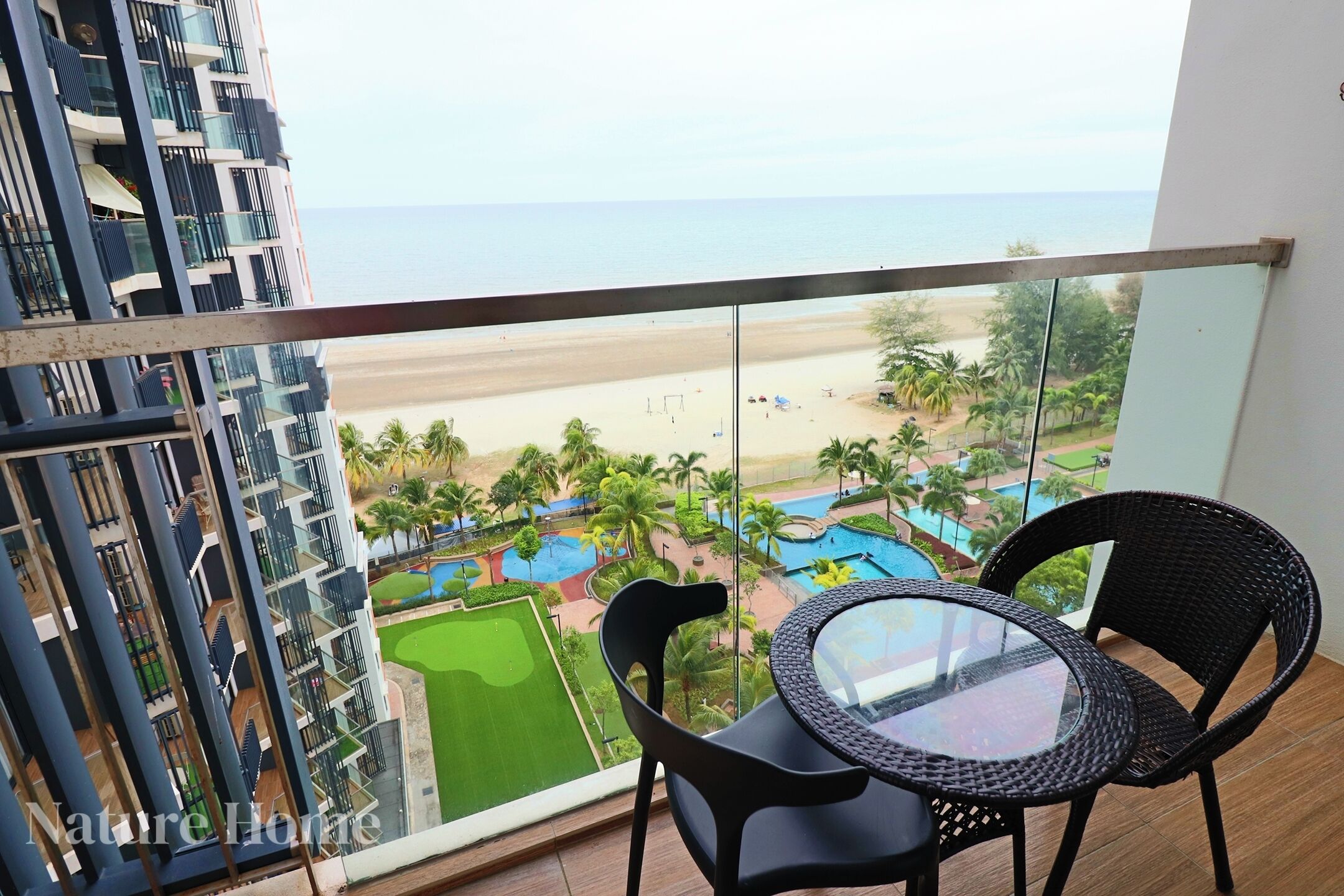A balcony with a view of a beach, a pool, and a golf course.