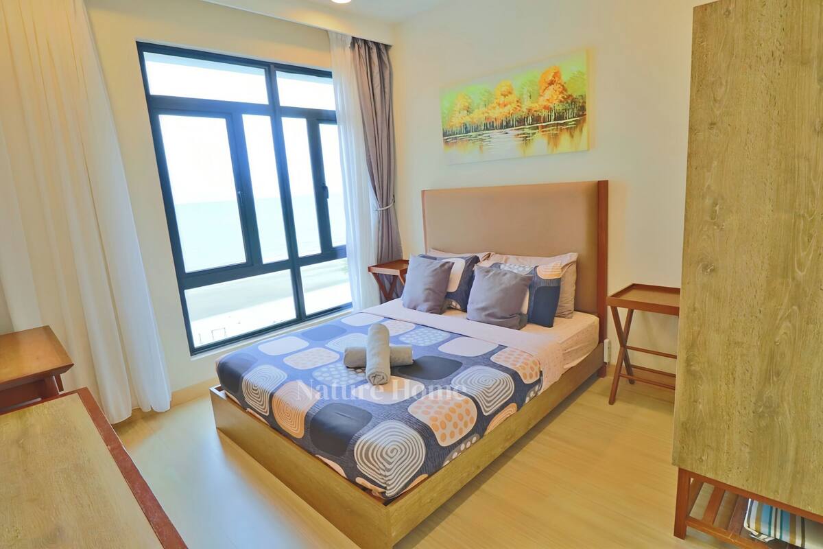 A bedroom with a large bed, a wooden nightstand, a small table, and a window with curtains.