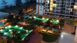 A high-rise hotel with multiple floors, a swimming pool area with green lighting, and a view of the ocean. - Timurbay Seafront Residences NatureHome (Kuantan)