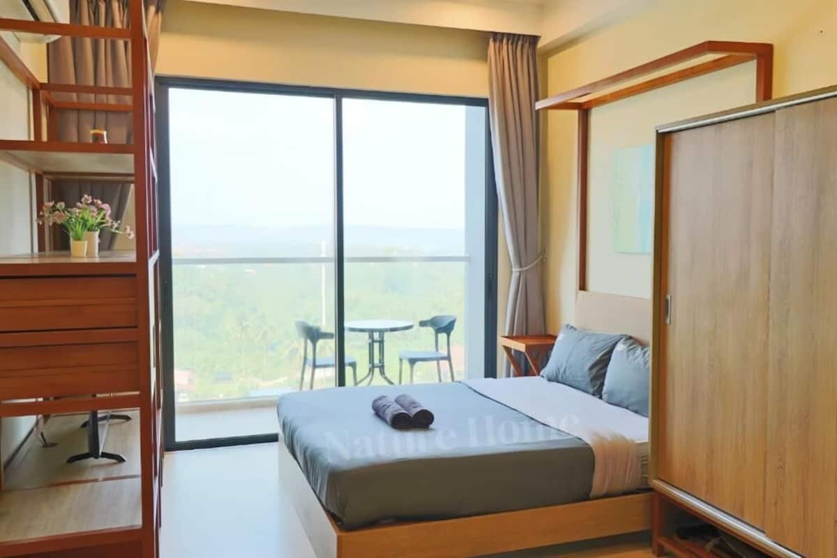 A hotel room with a large bed, a wooden wardrobe, a desk, and a balcony with chairs.
