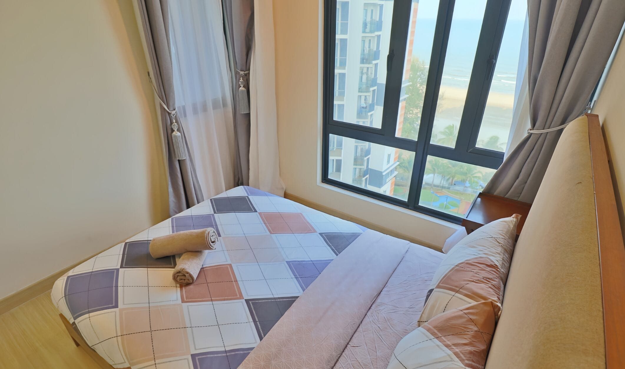 Une chambre avec une grande fenêtre, un lit recouvert d’une couvre-lit à motifs et une serviette enroulée posée sur le lit.