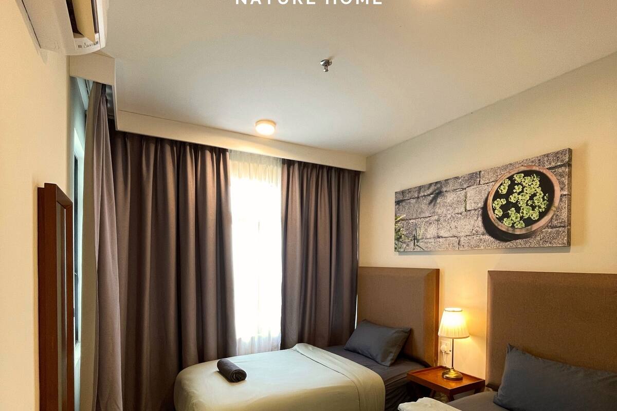 A hotel room with two beds, a nightstand with a lamp, a wall-mounted artwork, and a window with curtains.