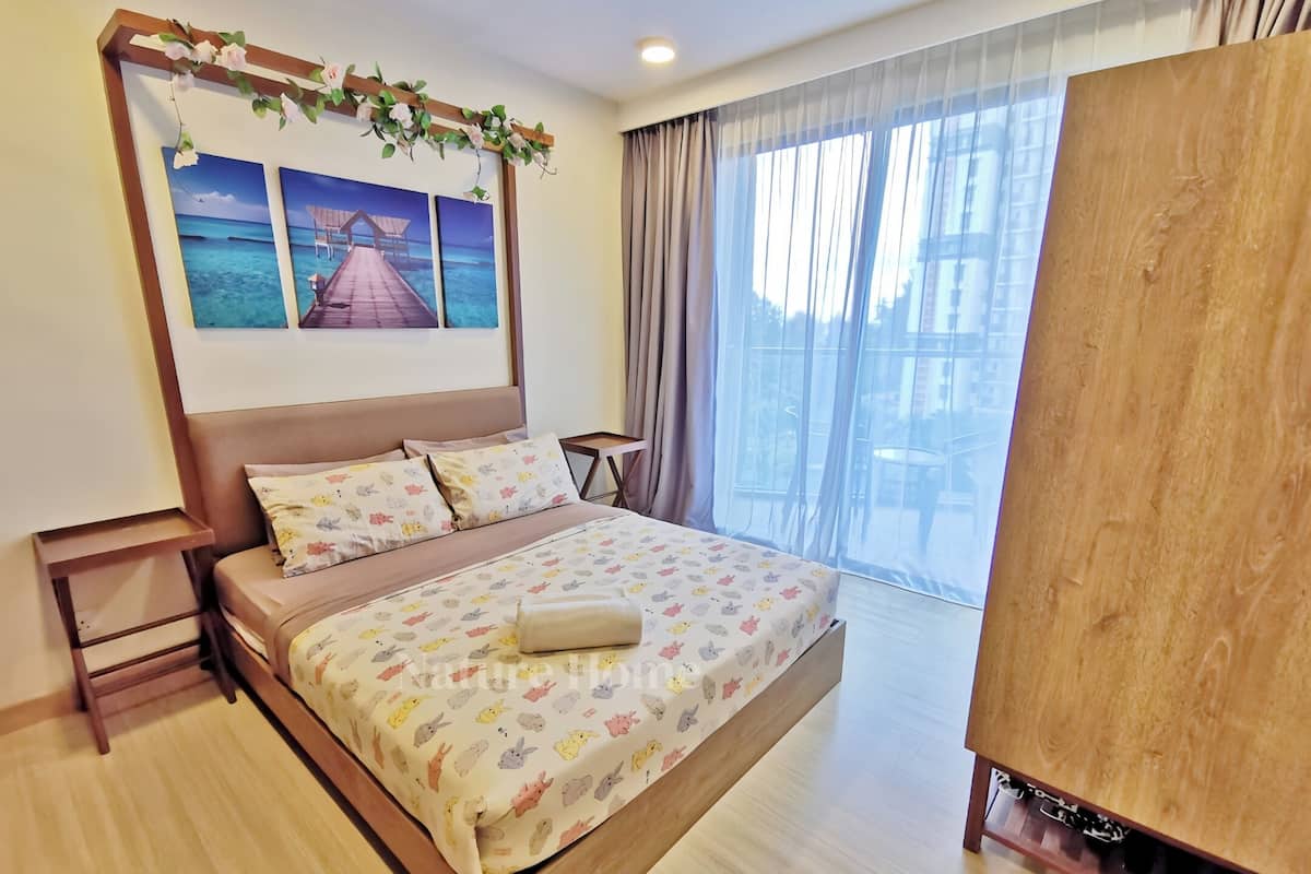 A hotel room with a large bed, a wooden headboard, a view of the sea through the window, and a small table by the window.
