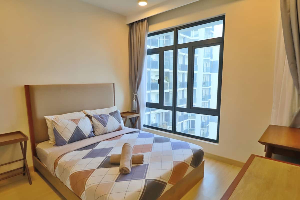 A hotel room with a large window, a bed with a patterned bedspread, and a wooden nightstand.