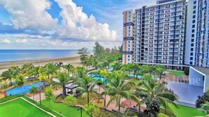 A high-rise building with multiple balconies, a pool area with palm trees, and a beach view. - Timurbay Seafront Residences NatureHome (Kuantan)