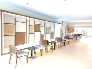 A modern interior with a row of chairs and tables, a light-colored floor, and a wall with geometric patterns. - Timurbay Seafront Residences NatureHome (Kuantan)